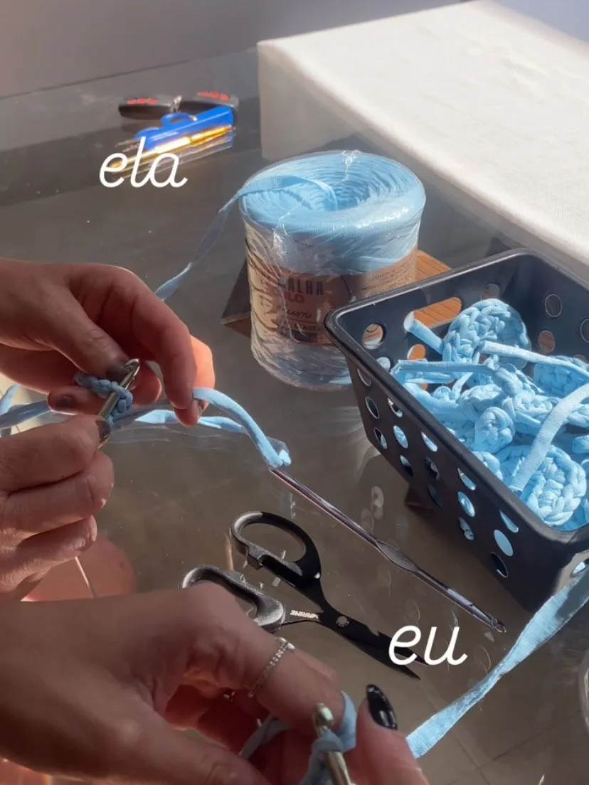 As mãos da mãe e da filha trabalhando o fio de malha azul na mesa do ateliê