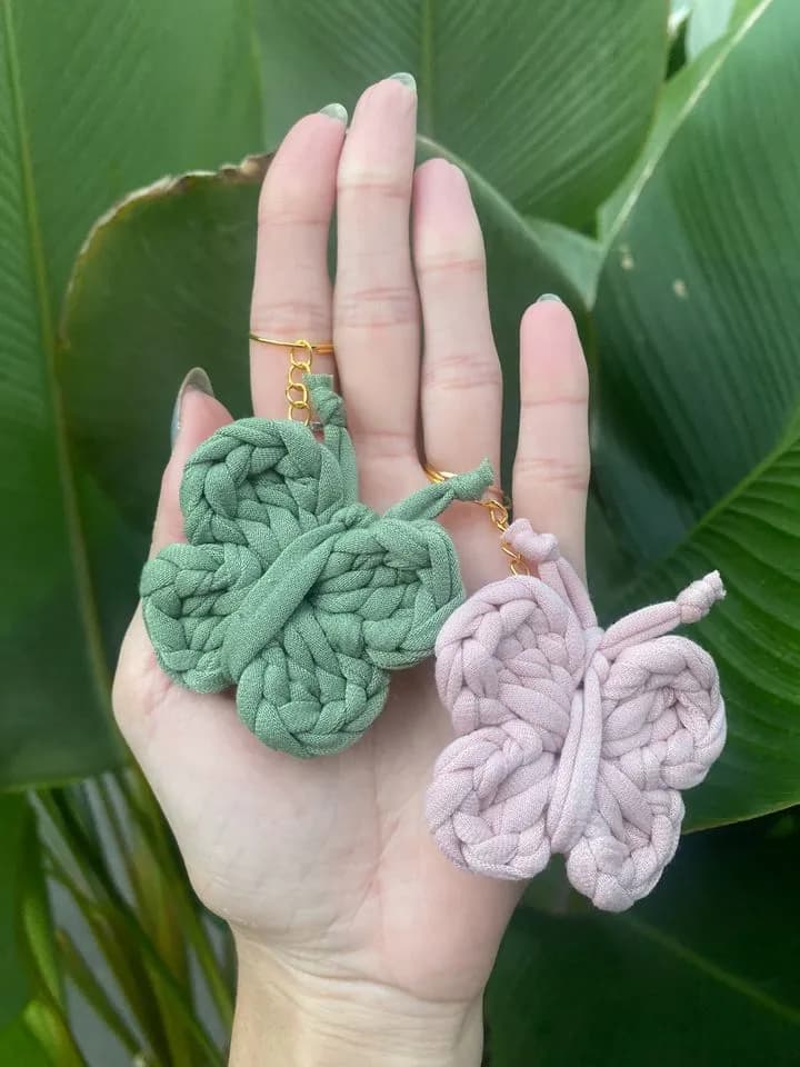 Duas borboletas de fio de malha, uma verde e uma lilás, na palma da mão
